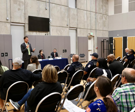 Zach Klein speaks into a microphone at a Block by Block meeting before an audience of residents and police.