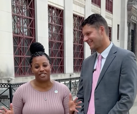 Zach Klein and Tiara Ross stand outside City Hall for a “Tuesday Tea” video. Ross gestures while speaking as Klein smiles beside her.