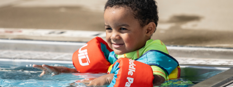 Child in swimming pool with orange floating devices on arms 