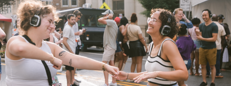 Two people outside with headphones on dancing and smiling 