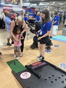 A mom and child play the golf game while a DCY team member helps during the Ohio State Fair.