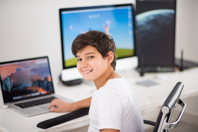 Preteen boy smiling as he sits in front of a computer.