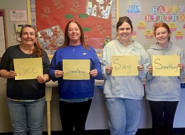 Four child care workers holding signs that say, "See Something Say Something."