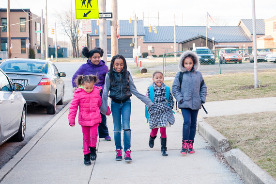 Group of five children wearing jackets and boots, walk towards the camera on a sidewalk.