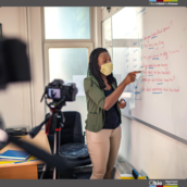 Teacher wearing a mask writing on a dry erase board.