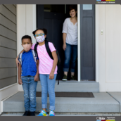 Elementary aged students standing on their home stoop wearing facial masks. 