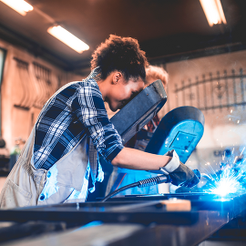 A woman uses welding material in a shop.