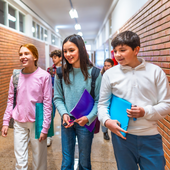 Students smile as they walk through a school hallway, talking together.