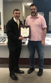 Auditor Stinziano stands with Moses Jewelers owner in front of a counter of watches while holding a True Transactions Award certificate. 