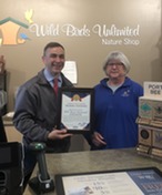 Auditor Stinziano stands holding a certificate with the manager of Wild Bird Center in front of the store sineage.. 
