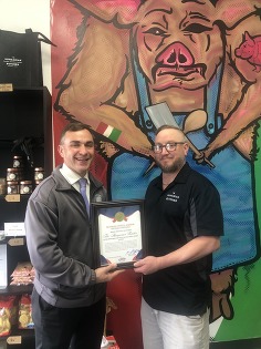 Auditor Stinziano presents a certificate to the Hungarian Butcher in front of a mural of a pig in a butcher apron inside of the Linworth store. 