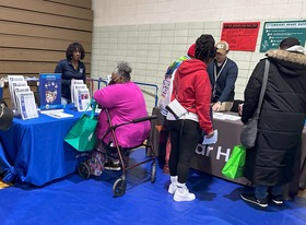 Vendors are arranged in a gymnasium behind tables with pamphlets at the Affordable Housing Resource Fair last spring.