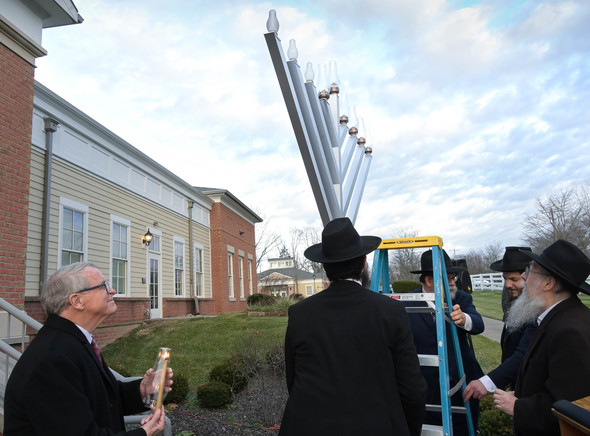 Governor DeWine holds the shamash candle before Rabbi Areyeh Kaltmann takes it to light five candles signifying the fifth night of Hanukkah.