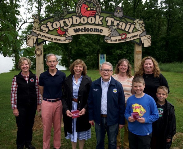 Governor DeWine, First Lady DeWine, ODNR Director Mertz, and others stand at the entrance of the new Storybook Trail in Rocky Fork State Park.