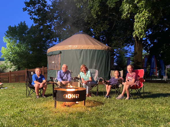 Governor DeWine, First Lady DeWine, and several of their grandkids sit outside by the fire in the ODNR Natural Resources Park.