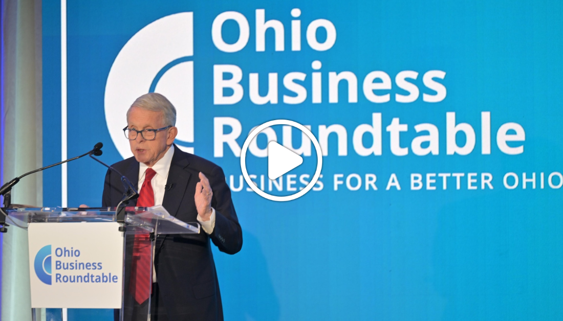 Governor DeWine speaking at a podium. In the background, a blue screen says "Ohio Business Roundtable"