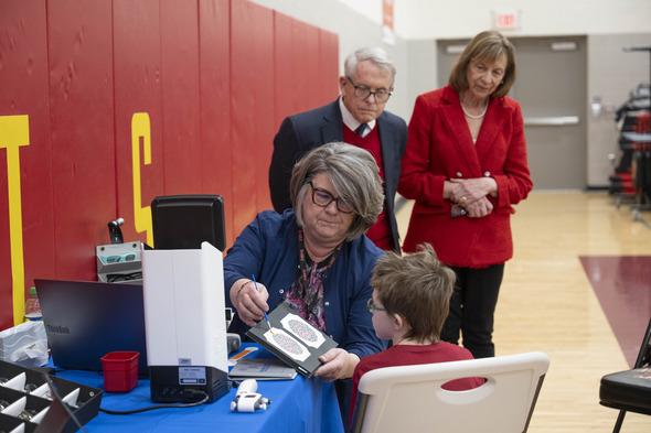Governor and First Lady look on while student receives eye exam