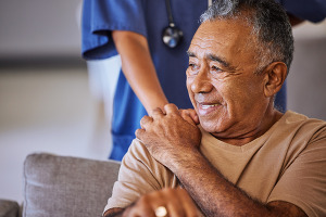 A man sitting in a chair, a nurse behind him puts her hand on his shoulder