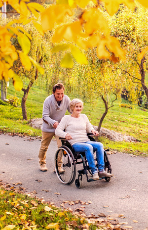 An older adult couple enjoying fall leaves, a man pushes a woman in a wheelchair