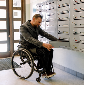 a man in a wheelchair opens a mailbox in an apartment building mail room