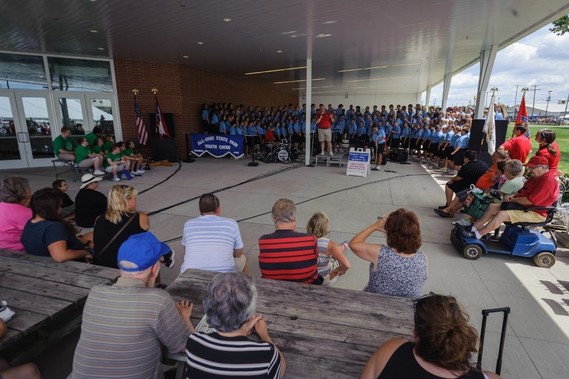 Families sitting at picnic tables listening to All-Ohio State Fair Youth Choir at State Fair pavilion