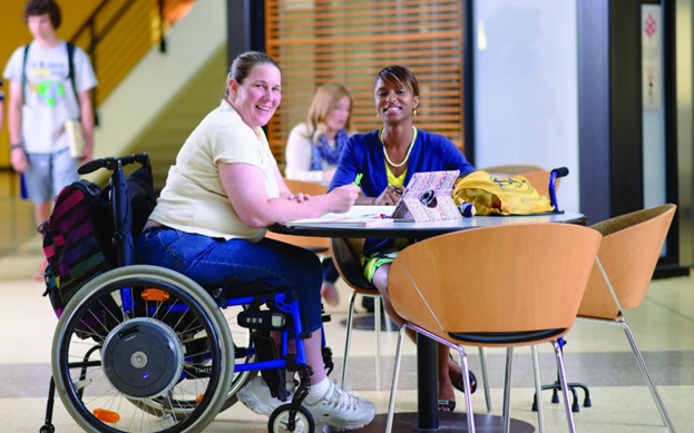 Female student in wheelchair sits with another female at a campus table