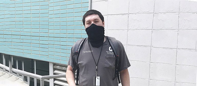 Photo of Justin Durkel with a mask in front of his building at OSU