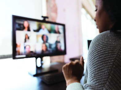 Woman in front of lap top with 9 people's faces on laptop