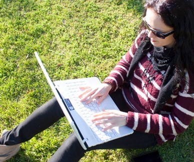 Girl sitting in grass with sunglasses on typing on a laptop