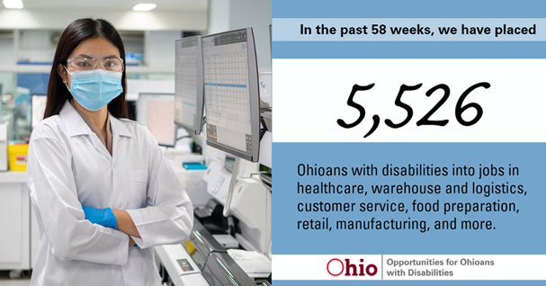 woman with long black hair wearing goggles and blue face mask and white coat and blue gloves standing with arms folded