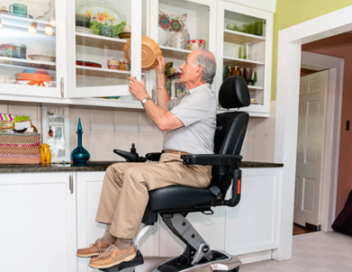 Photo of older gentleman in elevated wheelchair placing dish in cupboard