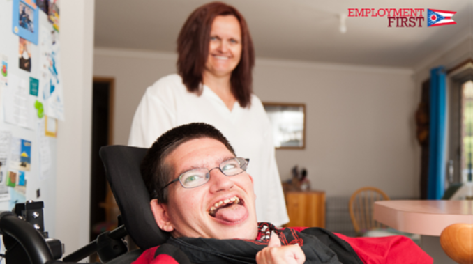 Photo of man in wheelchair making a silly face with woman behind him smiling