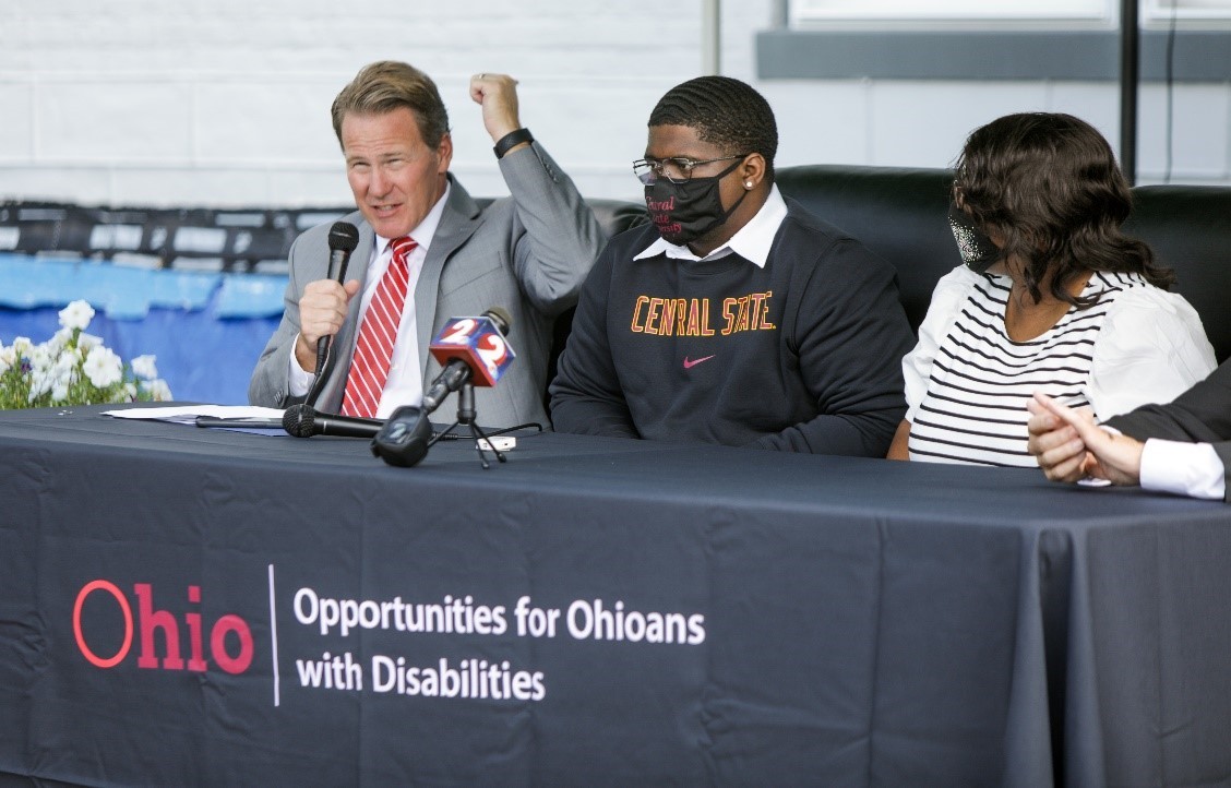 Photo of Lt. Governor Jon Husted speaking into microphone  and students Andre Green and  Lakysha Sager sitting at table at C2C event