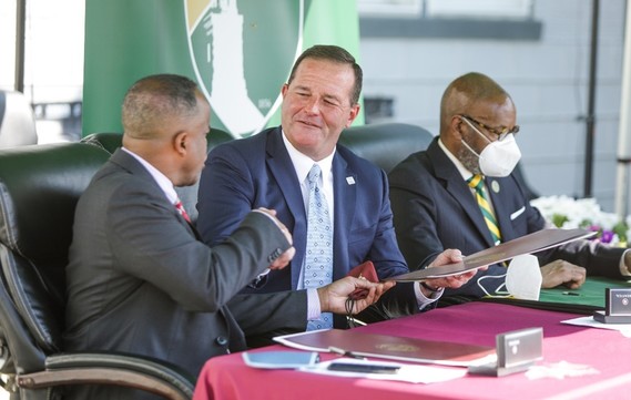 photo of Dr. Thomas and Director Miller shaking hands  with Dr. Pinkard also sitting at table