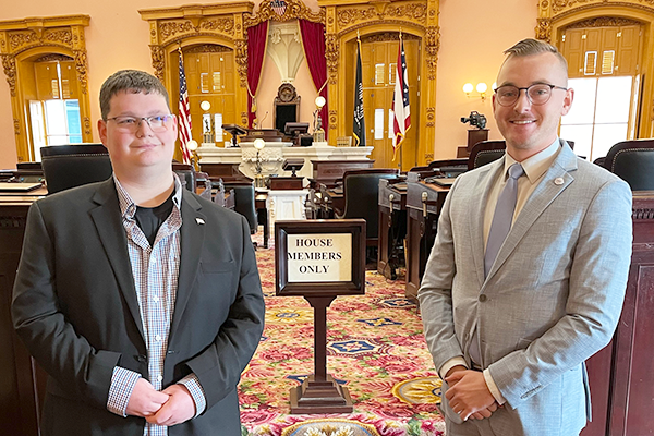 Two males wearing business attire stand smiling in front of the House Members Only sign.