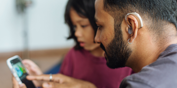 Man wearing hearing device and sharing his phone with a young female child.