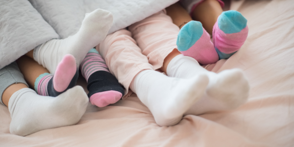 Various sized feet wearing socks sticking out from under a blanket.
