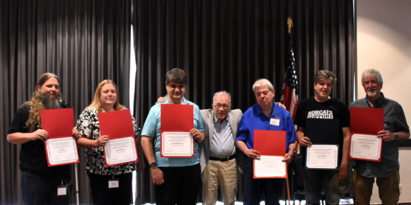 Seven individuals standing in a group, six of which are holding certificates.
