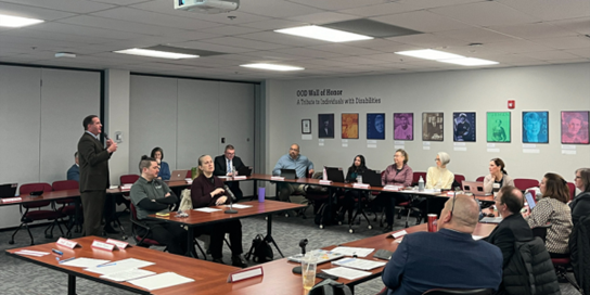 OOD Council meeting with individuals seated at tables and Director Miller speaking with a microphone.