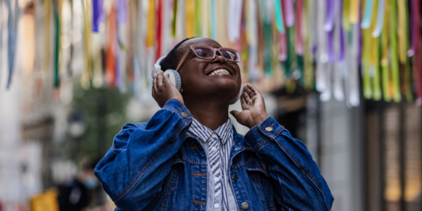 A person standing outside wearing headphones and smiling up at the sky.