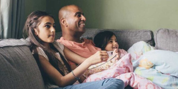 An adult and two children sitting on a couch together and looking at something off camera.