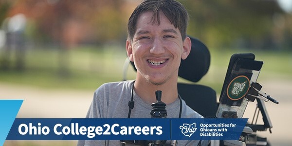 A person seated in a a mobility device smiling at the camera.