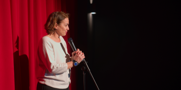 Woman with a long cane on a stage holding a mic.