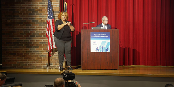 Lena Schmitz, ASL Interpreter, and Governor DeWine at a podium on stage.