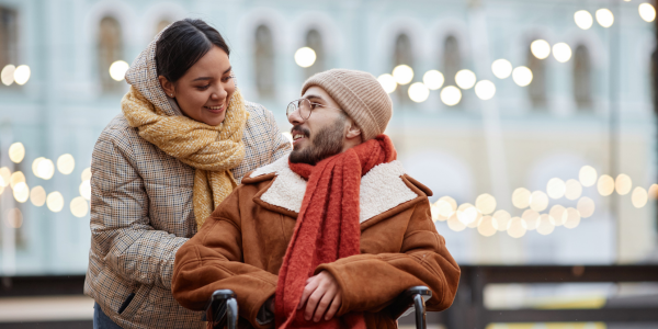 Young couple with a man using a wheelchair enjoying an outdoors, bundled in winer wear.