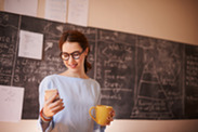 young teacher sending a text message while standing in her classroom