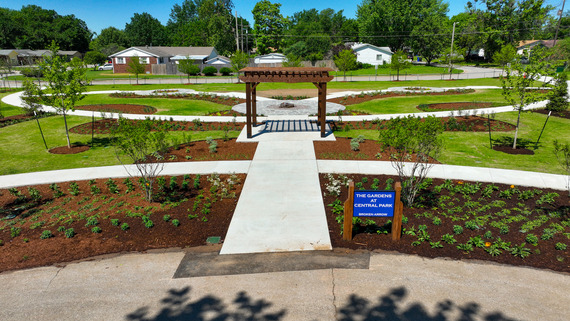 This is a picture of the entrance to The Gardens at Central Park. There is a pergola, various plantings and trees.
