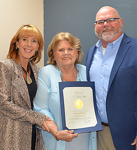 Three people with one woman in middle holding a certificate.