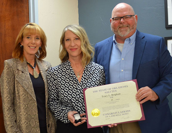 Three people with one person in middle holding a certificate.