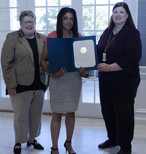 Three women with one holding an award.